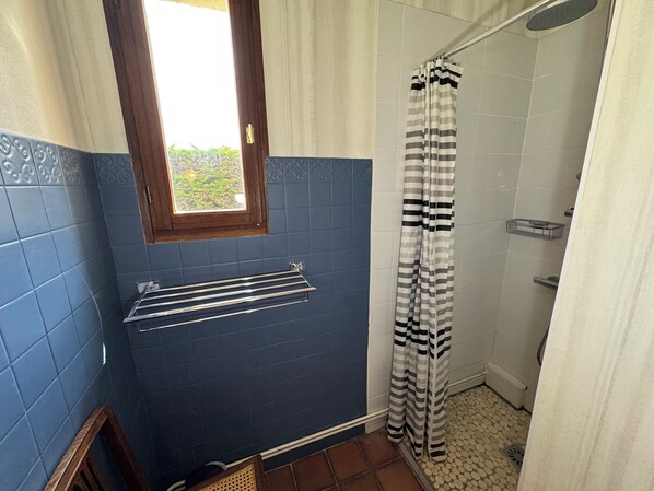 A bathroom with blue tiles, a window, a shower with striped curtains, and a towel rack. - Detached 3-bedroom house, 100 square meters, with a fenced-in yard (Fort-Mahon-Plage)