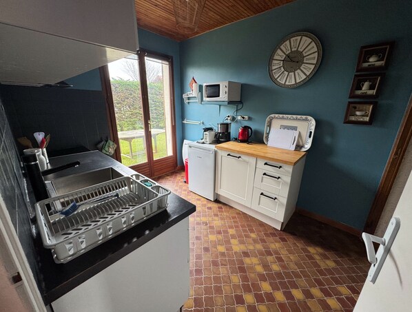 A compact kitchen with a sink, microwave, and a clock on the wall. - Detached 3-bedroom house, 100 square meters, with a fenced-in yard (Fort-Mahon-Plage)