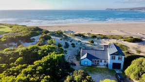 Una casa costera con un amplio balcón, rodeada de vegetación exuberante y una playa de arena.