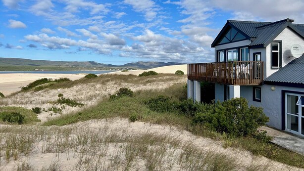 Una casa moderna con balcón que da a una playa y dunas.