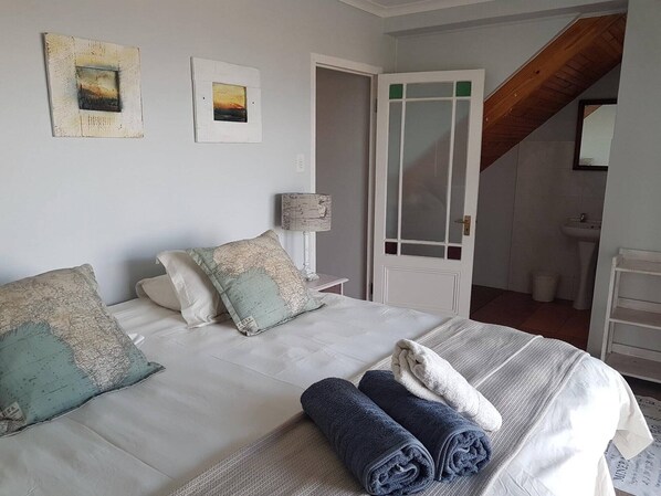 Un dormitorio con cama, almohadas, lámpara y vista al baño.