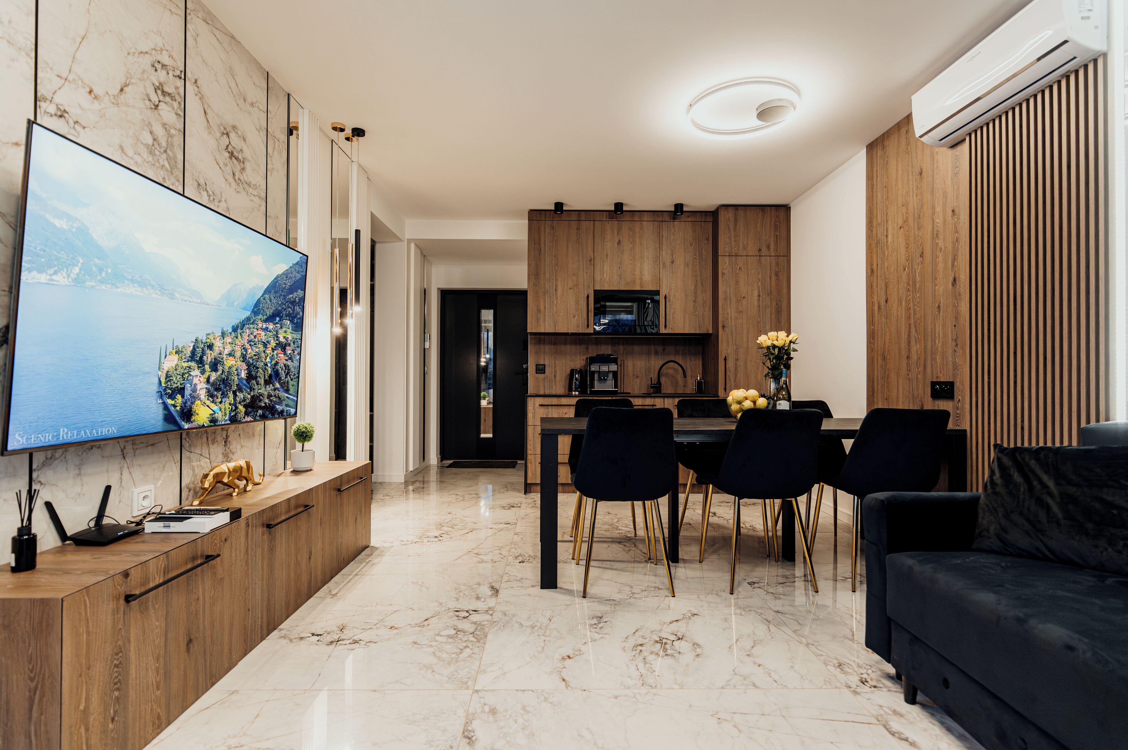A modern living room with a flat-screen TV, a dining area with a wooden table and chairs, and a black sofa.