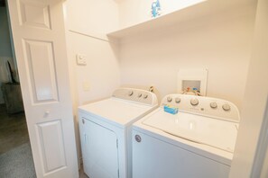 A laundry room with two white front-loading washers and dryers, a white door, and a shelf above the dryers.