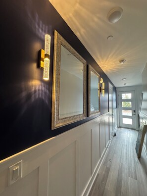 A hallway with dark walls, white wainscoting, and three large mirrors with light fixtures. - Luxury 4 bedroom townhome in charming Santa Rosa Beach, close to 30a (Santa Rosa Beach)
