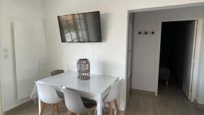 A modern dining area with a white table and chairs, a mounted TV, and a wooden floor. - Vacation home, Villa Hortense (Notre-Dame-de-Monts)