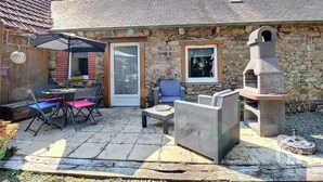 A stone building with a tiled roof, a patio with outdoor furniture, and a stone oven.