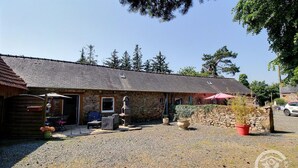 A rustic stone building with a gravel driveway, outdoor seating, and a barbecue area.