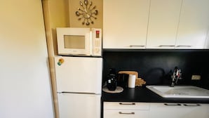 A compact kitchen with a microwave, refrigerator, sink, and a decorative wall clock.
