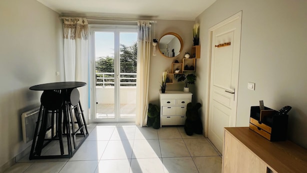 A room with a sliding glass door leading to a balcony, a round mirror, a small white dresser, and a wooden cabinet.