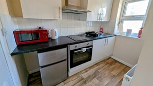 Une cuisine compacte avec des meubles blancs, un plan de travail noir, un micro-ondes rouge, une bouilloire et une fenêtre donnant sur un beau paysage.
