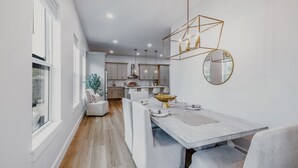 A modern kitchen with white cabinets, a dining area with a large table and chairs, and pendant lighting. - New! Alora: Gorgeous 4BR Beach Getaway w Game Room + Spa + Firepit (Santa rosa beach)