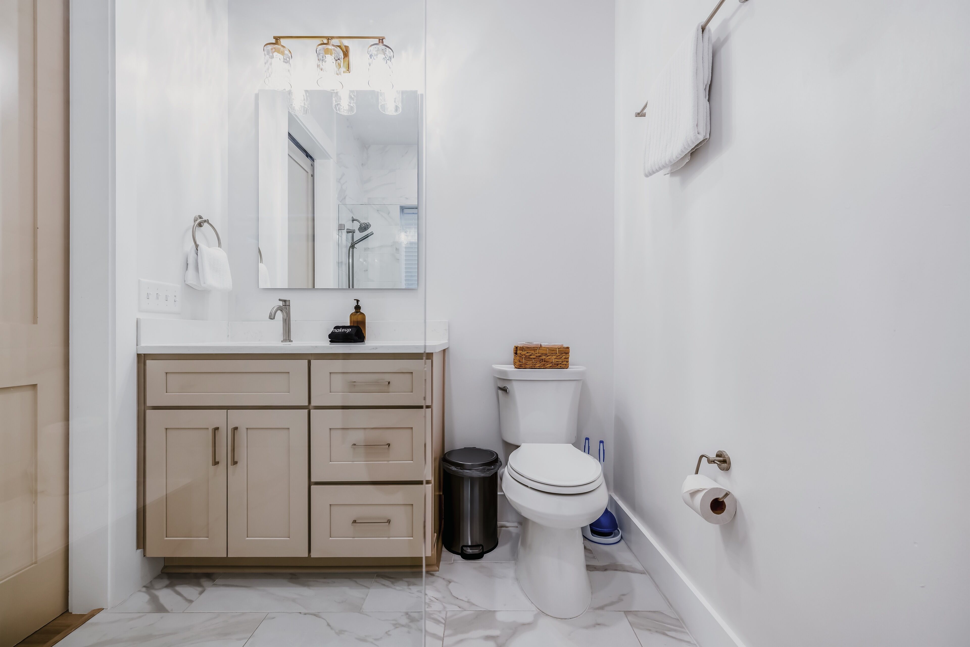 Un baño moderno con tocador blanco, inodoro y cubo de basura.
