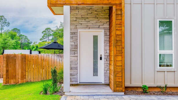 A modern house with a stone facade, a wooden deck, and a fenced backyard. - New! Alora: Gorgeous 4BR Beach Getaway w Game Room + Spa + Firepit (Santa rosa beach)