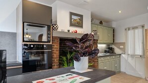 A modern kitchen with a brick fireplace, a built-in oven, and a dining area with a black table. - Gîtes de France® - La Lampèrierre (SAINT SAENS)