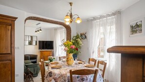 A dining area with a table set for four, a vase with flowers, and a television in the background. - Gîtes de France® - La Lampèrierre (SAINT SAENS)