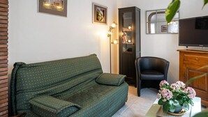 A living room with a green sofa, a black chair, a wooden cabinet, and a television. - Gîtes de France® - La Lampèrierre (SAINT SAENS)