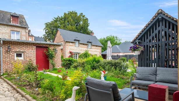 A garden with a stone building, a red door, and a wooden fence. - Gîtes de France® - La Lampèrierre (SAINT SAENS)