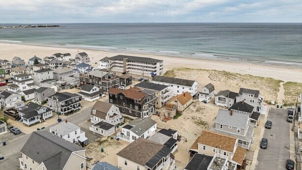 A coastal residential area with houses, a beach, and a pier in the background.