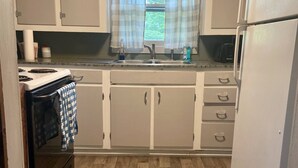 A compact kitchen with a stove, sink, and refrigerator. There is a window with curtains, and a patterned rug on the floor. - Charming 2-bedroom cabin in Big Clifty with WiFi, AC (Big Clifty)