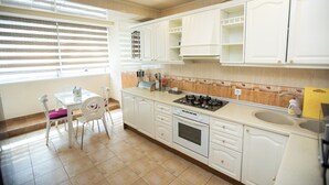 Una cocina con armarios blancos, una estufa a gas, un lavamanos y una zona de comedor con una mesa y sillas.
