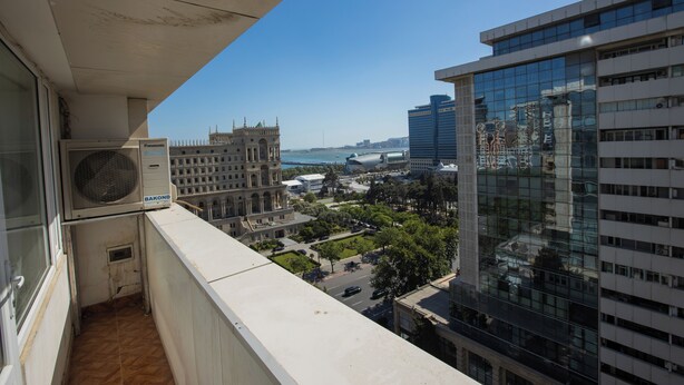 Un balcón con vistas a un paisaje urbano, que incluye un edificio histórico y rascacielos modernos.