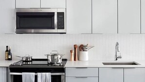 A modern kitchen with a stainless steel microwave, a gas stove, a sink, and white cabinetry. - Stylish, centrally-located condo in Uptown/West Village with high-end amenities! (Dallas)
