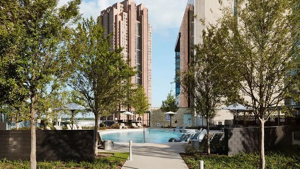 A modern building complex with a swimming pool, surrounded by trees and outdoor seating areas. - Stylish, centrally-located condo in Uptown/West Village with high-end amenities! (Dallas)