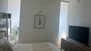 A bedroom with a bed, a TV, a ceiling fan, a framed picture on the wall, and a window. - Stylish, centrally-located condo in Uptown/West Village with high-end amenities! (Dallas)