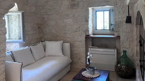 A cozy room with a stone wall, a white sofa, a small table with a vase, and a window with a view. - 15' to Monopoli, 10' to Capitolo Sea, 10/20' to all places in Valle D'Itria (Puglia)