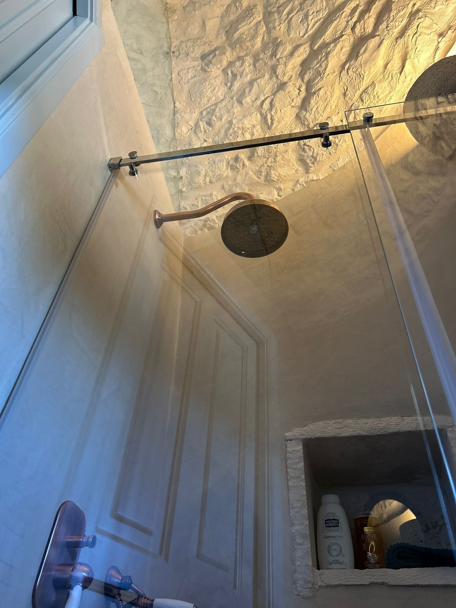 A bathroom with a shower, a door, and a shelf with toiletries.