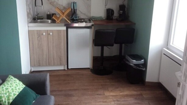 Une cuisine compacte équipée d’un évier, d’un four à micro-ondes et d’un petit réfrigérateur. On y trouve un meuble en bois et un plan de travail avec un porte-couteaux. Deux tabourets de bar sont placés près du comptoir.