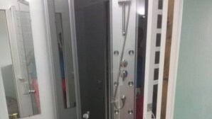 Un receveur de douche d’angle avec une porte en verre, un pommeau de douche et un flexible de douche.