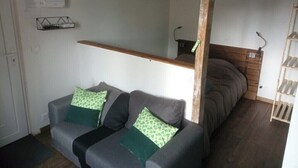 Une pièce avec un canapé gris, une tête de lit en bois, une étagère et un plancher en bois.