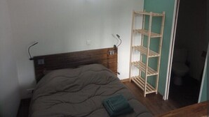 Une chambre avec une tête de lit en bois, un lit recouvert d’une couverture marron et une étagère en bois adossée au mur.