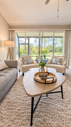 A modern living room with a large window, two sofas, a coffee table, and a floor lamp. - Charming 2 BR condo with golf course views in North Tampa! Snowbirds welcome! (Tampa)