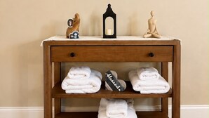 A wooden vanity with a round mirror, two decorative items, and three shelves holding folded towels. - Charming 2 BR condo with golf course views in North Tampa! Snowbirds welcome! (Tampa)