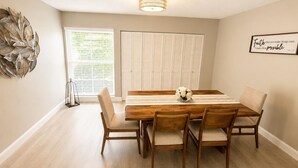 Un comedor con mesa y sillas de madera, un adorno en la pared y una ventana con persianas.