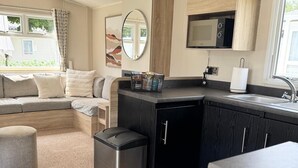 Un espacio habitable compacto con kitchenette, un sofá, un cesto de basura pequeño y una ventana con cortinas.