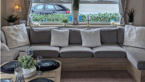 Un salón acogedor con sofá, una mesa de comedor preparada con platos y vasos, y vistas a un coche a través de amplias ventanas.