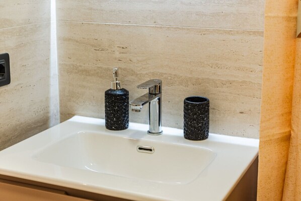 Un lavabo con grifo cromado, dos dispensadores de jabón negros con motas y una encimera blanca.