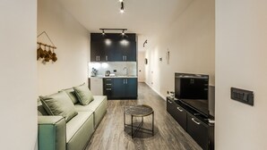 Una sala de estar moderna con sofá, mesa de centro, televisión y área de cocina con armarios y encimera.