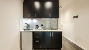 Una cocina compacta con armarios oscuros, una encimera blanca, un lavabo y un refrigerador pequeño.