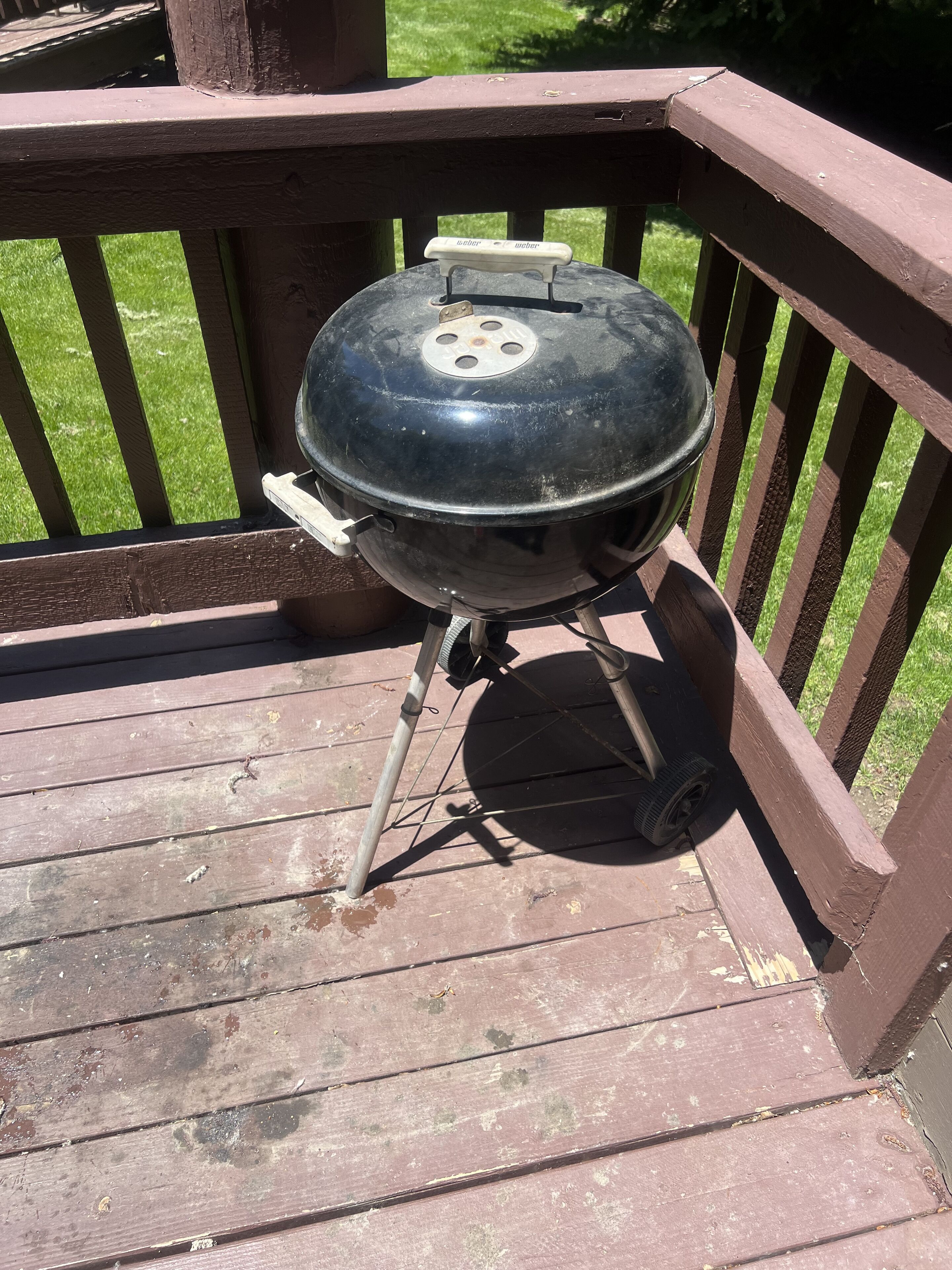 A portable grill on a wooden deck with railings.