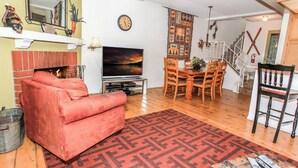 A living room with a red sofa, a TV, a fireplace, a dining area with wooden chairs, and a staircase. - Brown Bear's Den (Big Bear Lake)