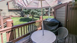 A deck with a table and chairs, an umbrella, and a barbecue grill. - Brown Bear's Den (Big Bear Lake)