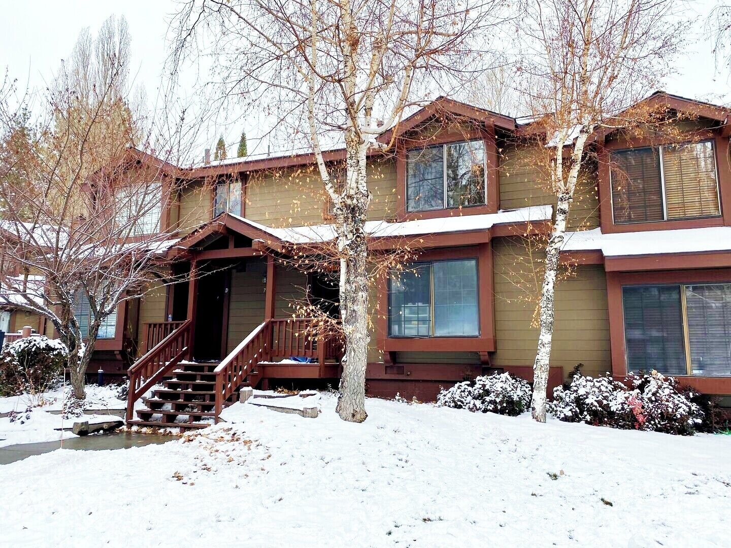 A two-story house with a front porch, a staircase, and a snow-covered yard.