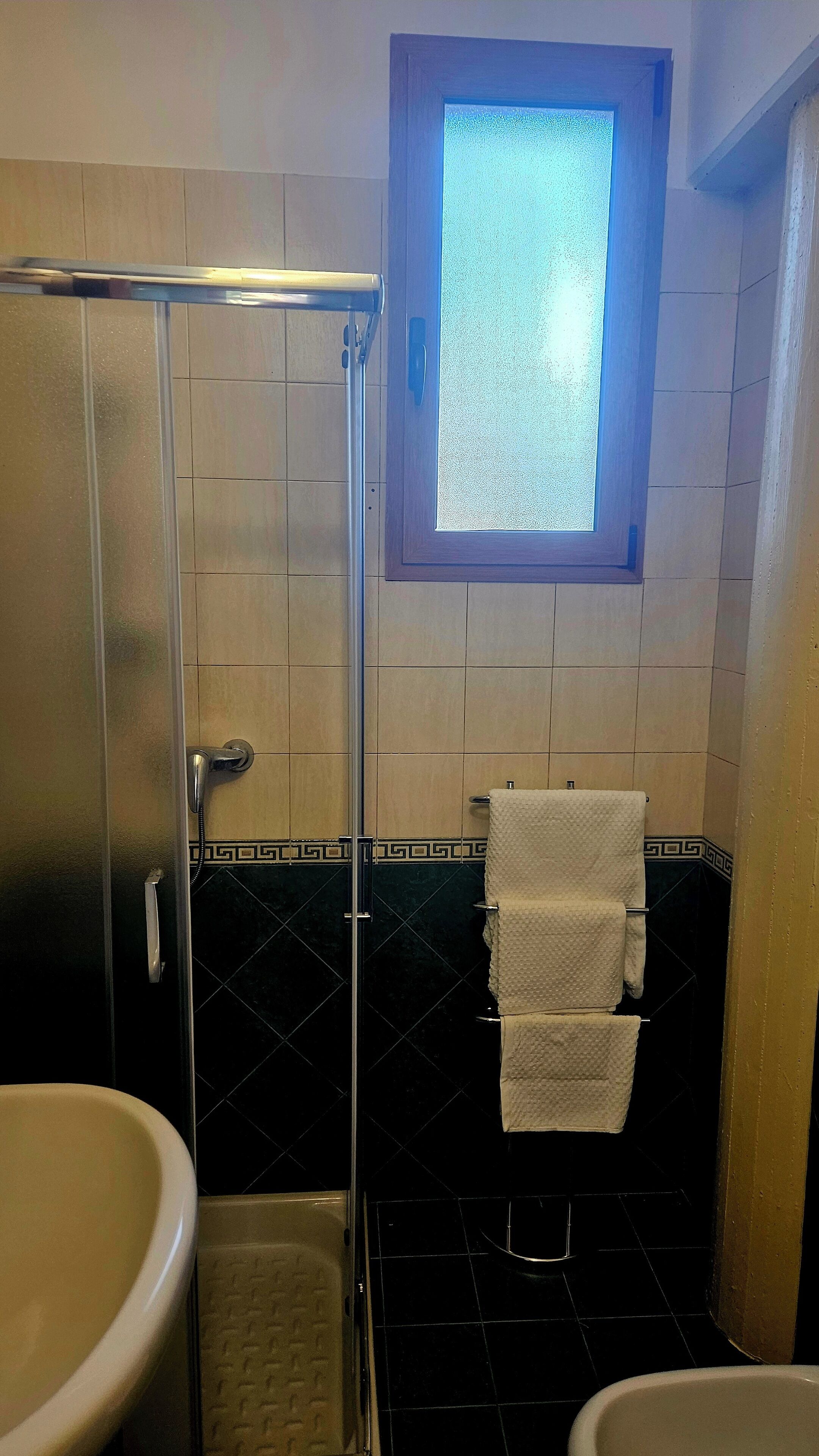 Ein Badezimmer mit Duschkabine aus Glas, einem Fenster und einem Fliesenboden.