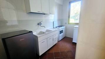 Une cuisine de taille réduite avec des meubles blancs, un évier, une cuisinière et un réfrigérateur.
