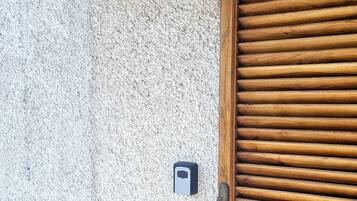 A textured wall with a black lantern, a wooden door, and a security keypad.