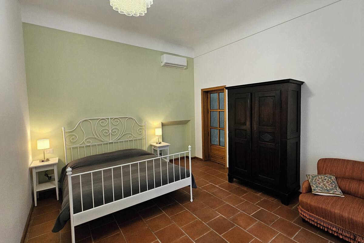 A bedroom with a bed, bedside lamps, a wardrobe, and a sofa.